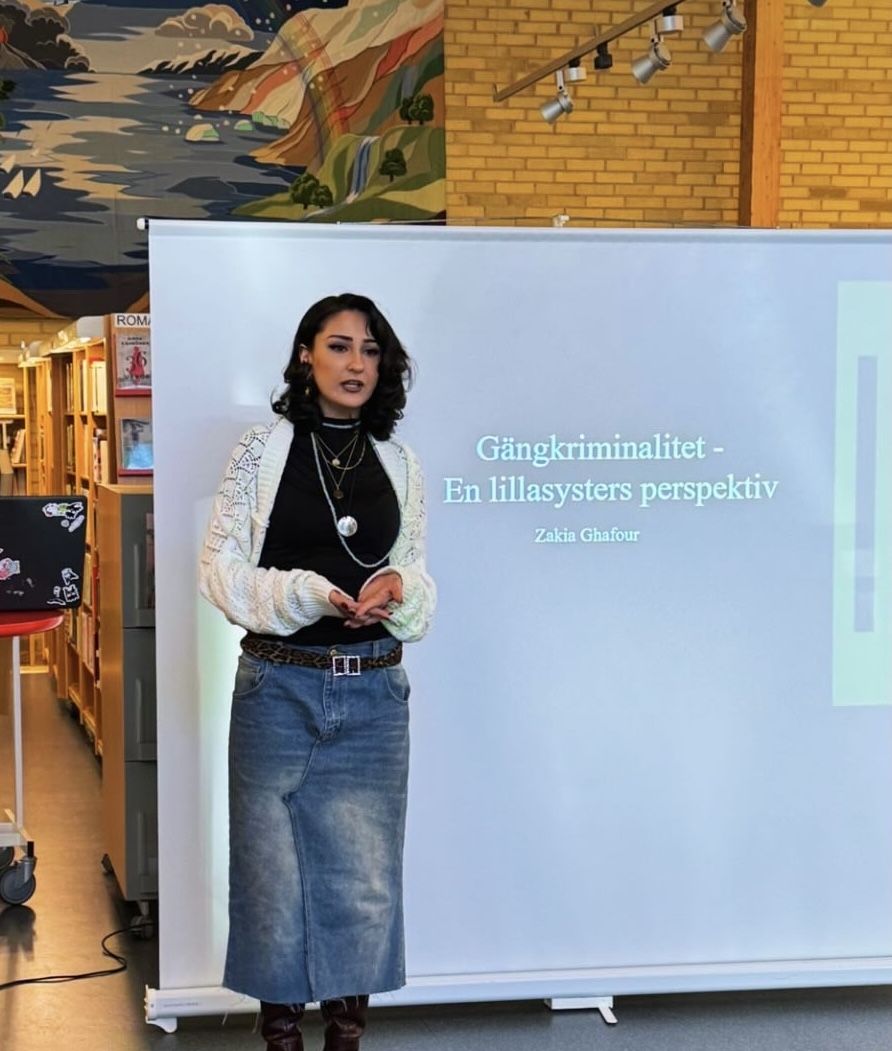 Zakia Gafour föreläser framför en skärm med texten Gängkriminalitet – En lillasysters perspektiv.